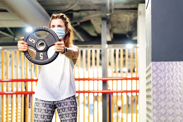 woman lifting weights at the gym with a mask