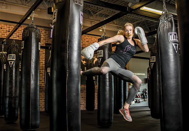 Sarah Krotz, a coach at TITLE Boxing Club Woodbury, kicks a punching bag.