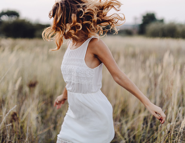 A woman with frizzy hair runs through a field during a hot, humid summer day.