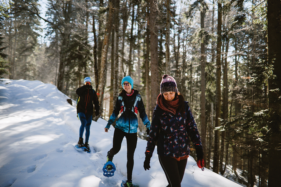 Active winter vacation in the snowy mountains. People snowshoeing - hiking using the snow shoes through the forest.