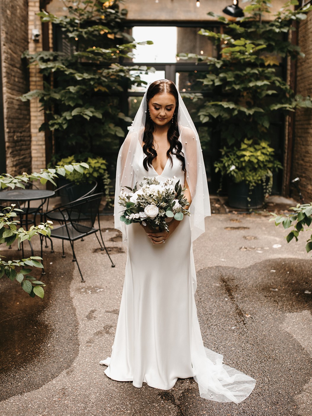 The bride’s lustrous satin gown from Vow’d Weddings was altered and customized by Heather Baldridge from Custom Sewing by Heather, who added satin buttons—flown in from Serbia—down the back of the gown. The look was paired with a chapel-length, angel-cut pearl veil from Tailored Tulle, pearl-drop earrings and white, satin heels, featuring dazzling bows. In the evening, the veil was exchanged for pearl gloves, also from Tailored Tulle.