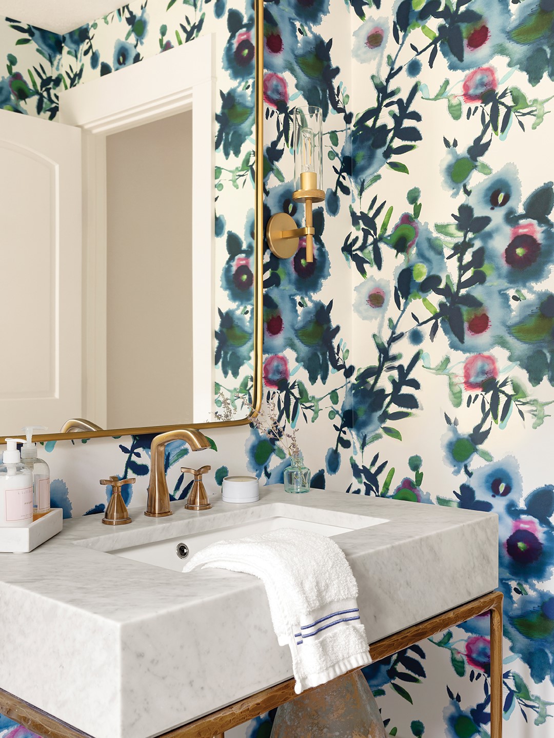 Although Becca Hall and the homeowner explored several wallpapers, they landed on a standout design from Thibaut. “We loved how the watercolor florals tied into the blue theme carried throughout the home, yet brought a completely fresh energy,” Becca Hall says. The powder bathroom, featuring the print, could’ve easily felt claustrophobic; instead, Hall intentionally balanced the wallpaper with simpler elements such as the lighting and fixtures.