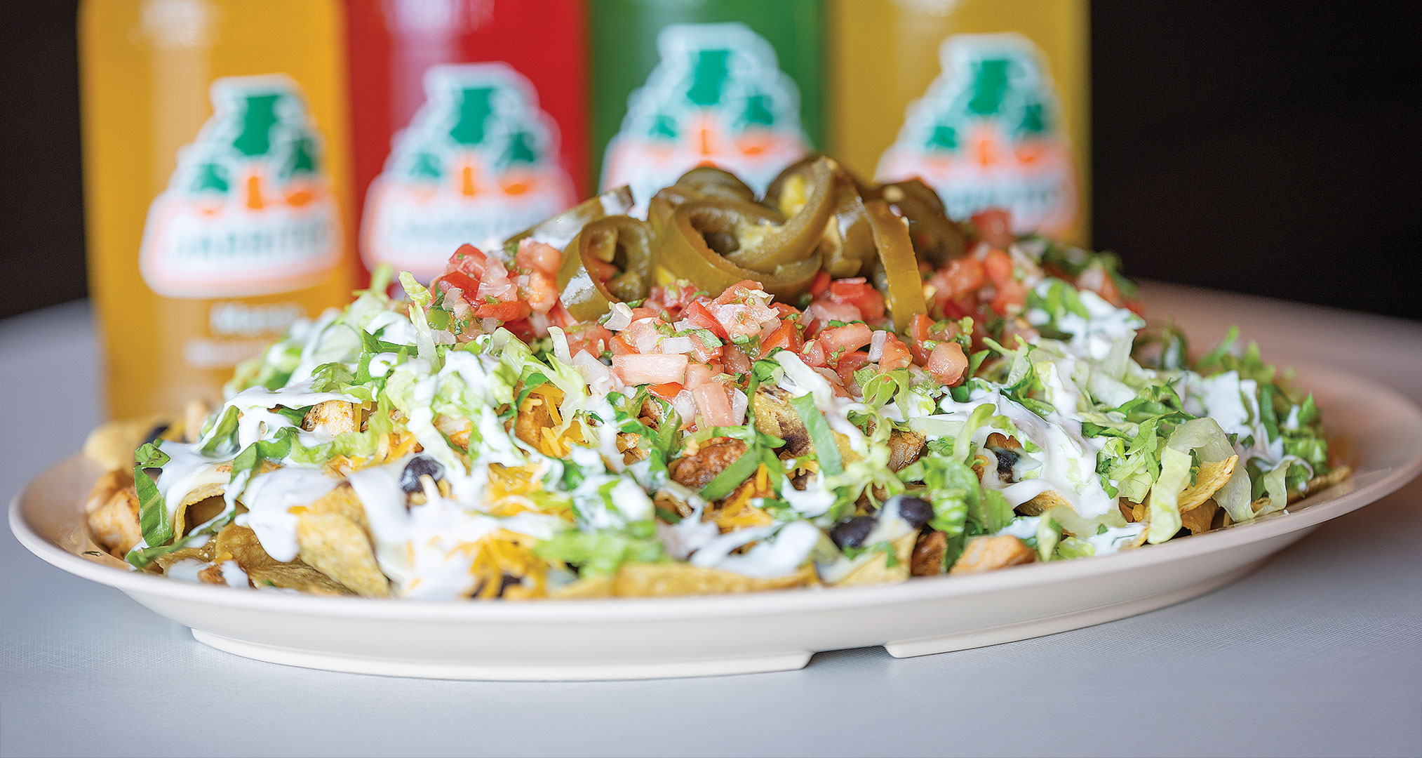 The Nachos are topped with black beans, queso dip, cheese, lettuce, sour cream, jalapeños, pico de gallo and customer’s choice of salsa and meat.